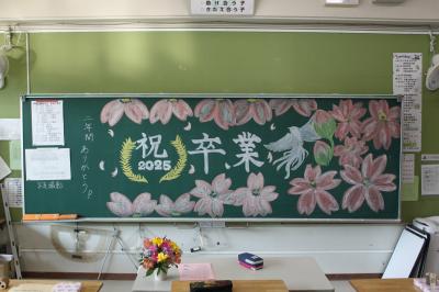 6年2組の黒板。桜の絵が描かれており「祝　卒業　二年間ありがとう」と書いてある。