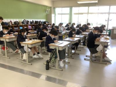 作図をしている児童を写した写真です。教室の右前方から後方に向けて全体を撮っています。ほとんどの児童がノートを見て作図をしています。小数の児童が顔を上げて教師が作図をした黒板を見ています。